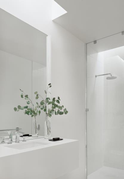 Современная белая ванная комната с потолочным окном, подчеркивающим туалетный столик, и стеклянной перегородкой от пола до потолка, отделяющей душ.
