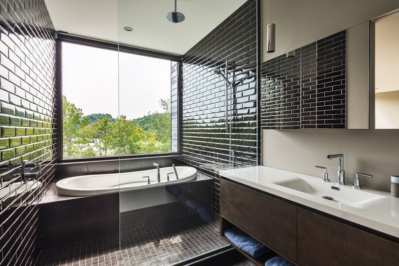 В этой ванной комнате есть душ и встроенная ванна, разделенные стеклянной перегородкой, а черная плитка привлекает внимание к виду с вершины деревьев снаружи.