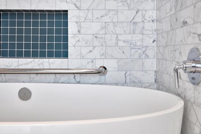 Современная ванная комната с белой ванной, серой мраморной плиткой метро и нишей для стеллажей, выложенной квадратной бирюзовой плиткой.