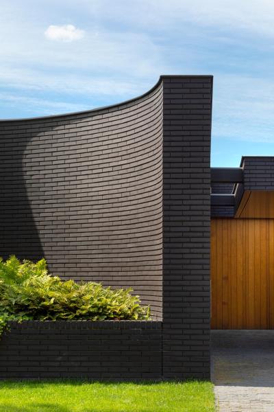 Фасад этого современного дома из черного кирпича имеет изгибы и большие встроенные вазоны, которые подчеркивают пышную зелень.