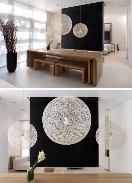 Черная перегородка комнаты (или перегородка) создает поразительный фон для трех белых подвесных светильников над деревянным обеденным столом.