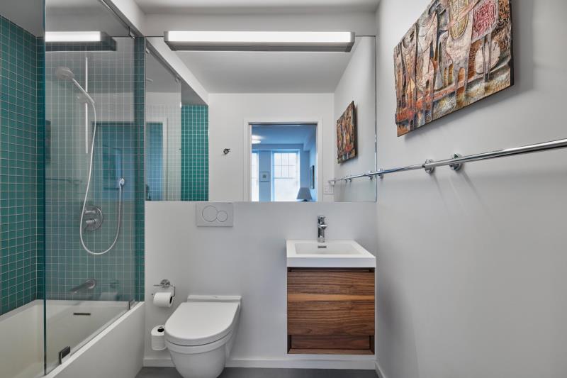 Современная ванная комната с ярко-белыми стенами, простой деревянный туалетный столик с белой раковиной и совмещенный душ / ванна с квадратной бирюзовой плиткой на стенах.