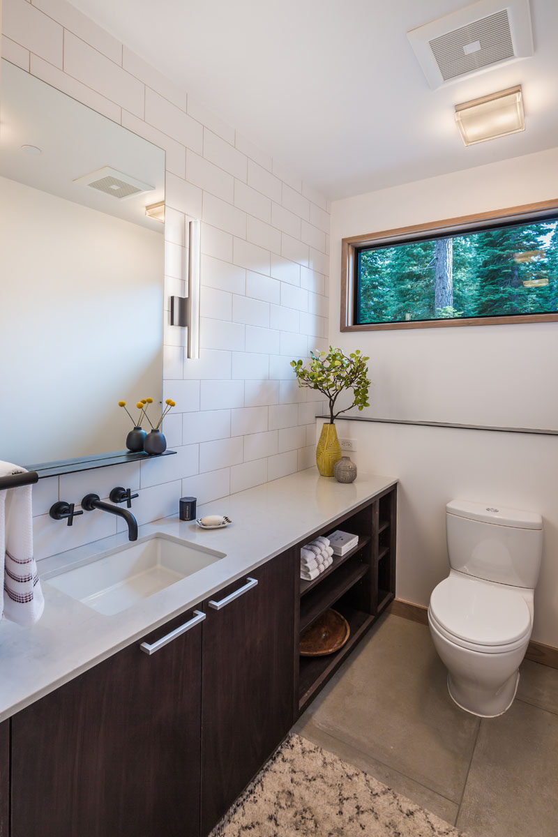 В оформлении ванной комнаты использована белая плитка метро и темный туалетный столик с несколькими открытыми полками.