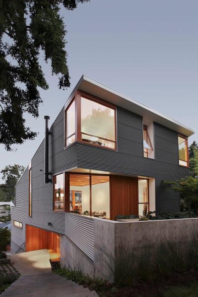 Современный дом с гофрированным металлическим сайдингом, бетонными элементами и деревянными оконными рамами.