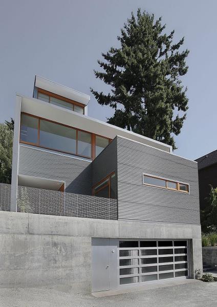 Современный дом с гофрированным металлическим сайдингом, бетонным фундаментом и деревянными оконными рамами.