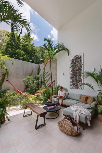Гостиная на открытом воздухе с удобным диваном и гамаком в окружении тропических растений.