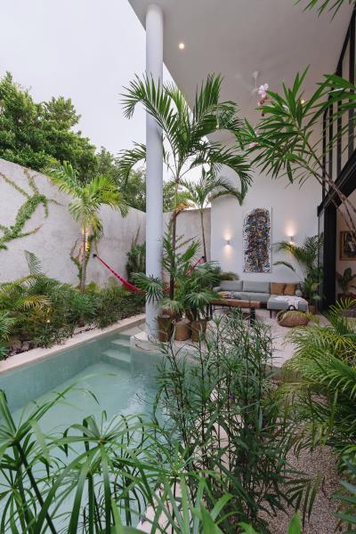 Небольшой дом с открытой гостиной, тропическими растениями и небольшим бассейном.