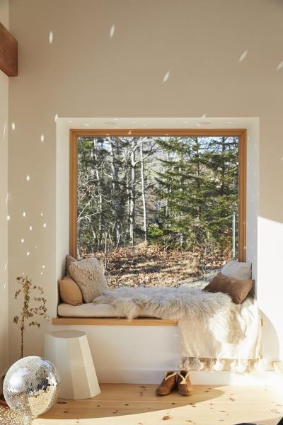 Уютное сиденье у окна с видом на деревья, мягкие подушки и одеяла, а также зеркальный шар, рассеивающий свет.