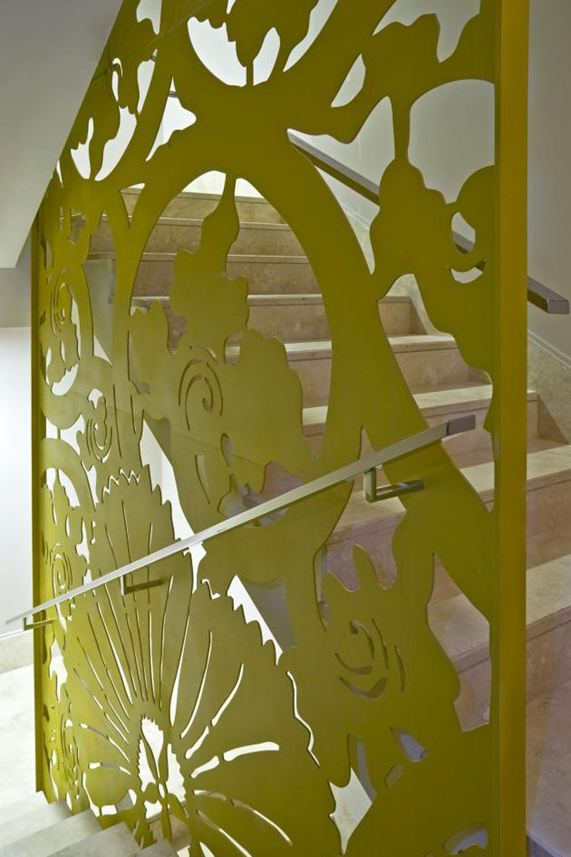 Металлический лист был вырезан лазером и окрашен в зеленый цвет, чтобы создать художественный цветочный принт, который служит одновременно ограждением для лестницы и художественной инсталляцией, на которую можно смотреть, поднимаясь и спускаясь по лестнице.