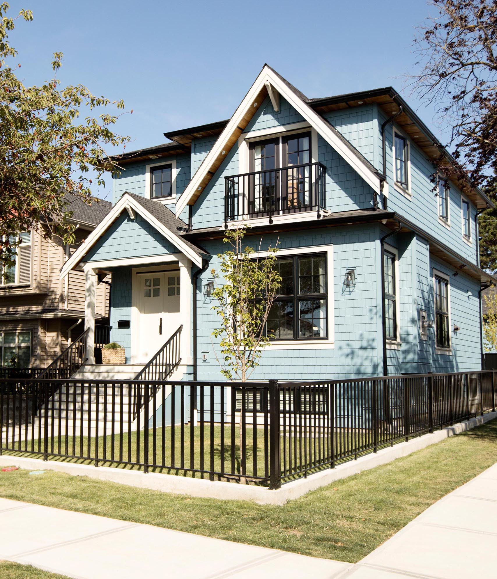 Современный голубой дом с белой отделкой и контрастным черным забором, перилами и оконными рамами.