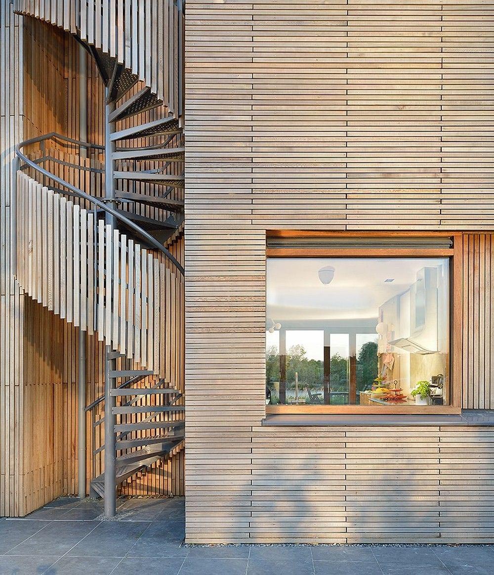 В современном деревянном доме есть внешняя винтовая лестница, покрытая деревянными рейками.