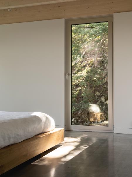 Из высокого окна этой современной спальни открывается вид на лес.