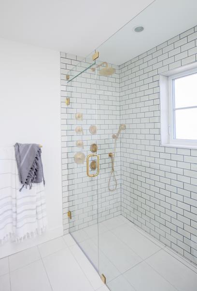 Современный душ с золотой фурнитурой, белой плиткой метро и контрастной темной затиркой.