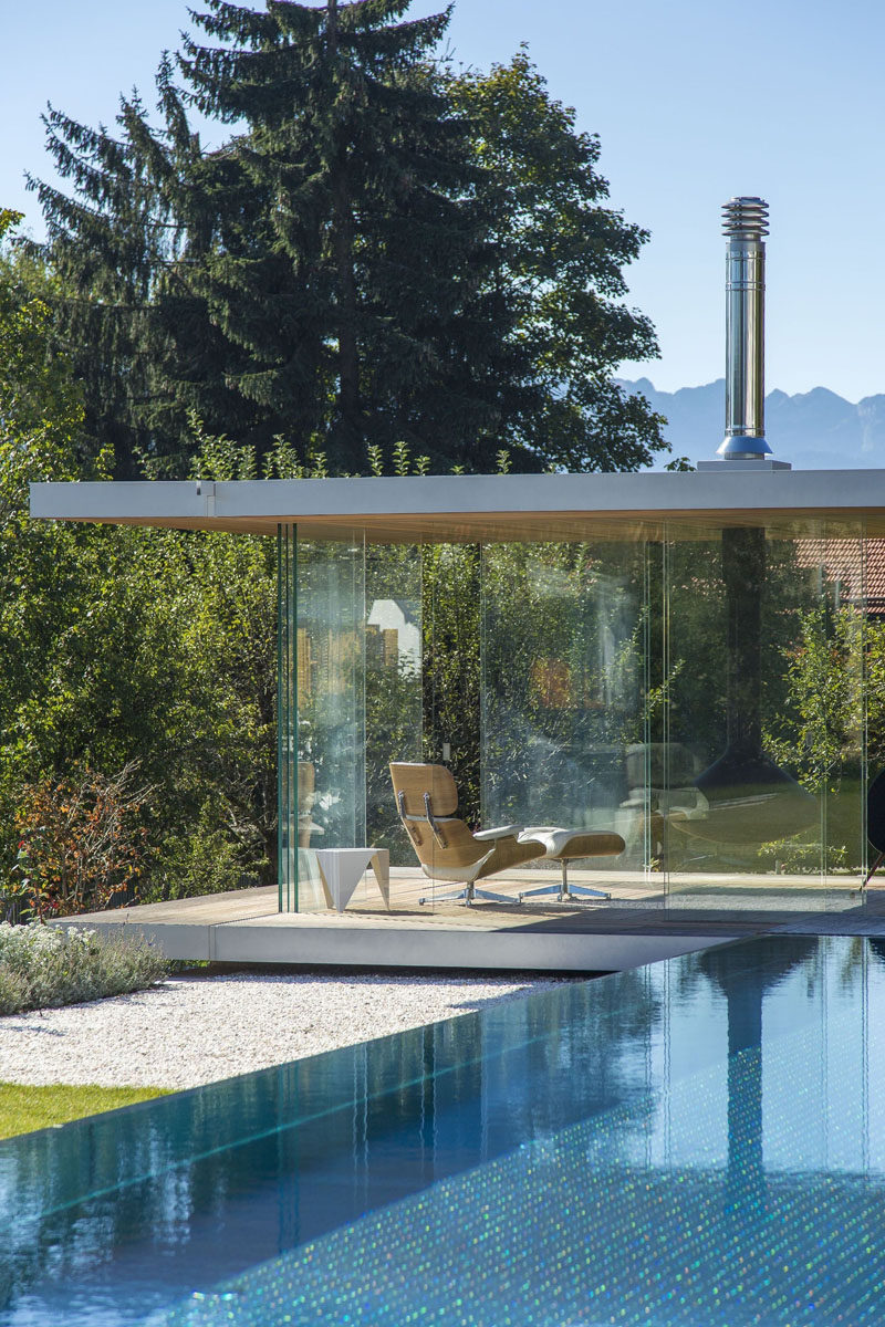 Современный стеклянный дом у бассейна имеет панорамный вид, раздвижные двери со всех сторон, подвесной камин и скрытый холодильник в полу. 