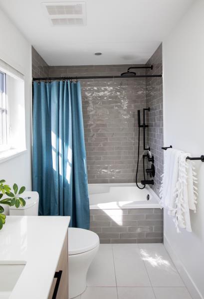 Современная ванная комната с отделанным серым кафелем душем, черной фурнитурой и синей занавеской.