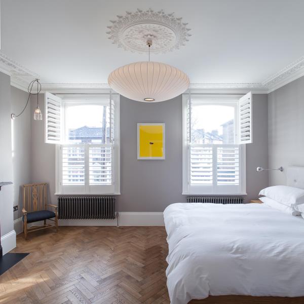 Современная спальня с серыми стенами, украшенными белой отделкой и оконными ставнями.