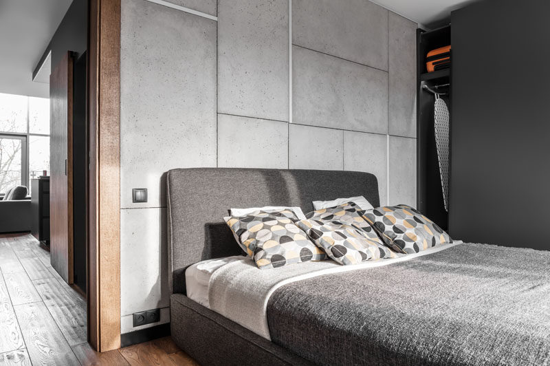 Современная спальня с бетонной акцентной стеной и темно-серым каркасом кровати.