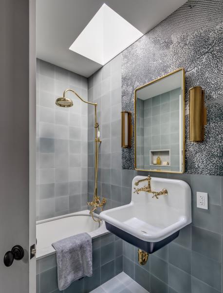 Ванная комната с плавающим туалетным столиком, золотой фурнитурой и смесителем, а также серыми плиточными стенами и окантовкой ванны.