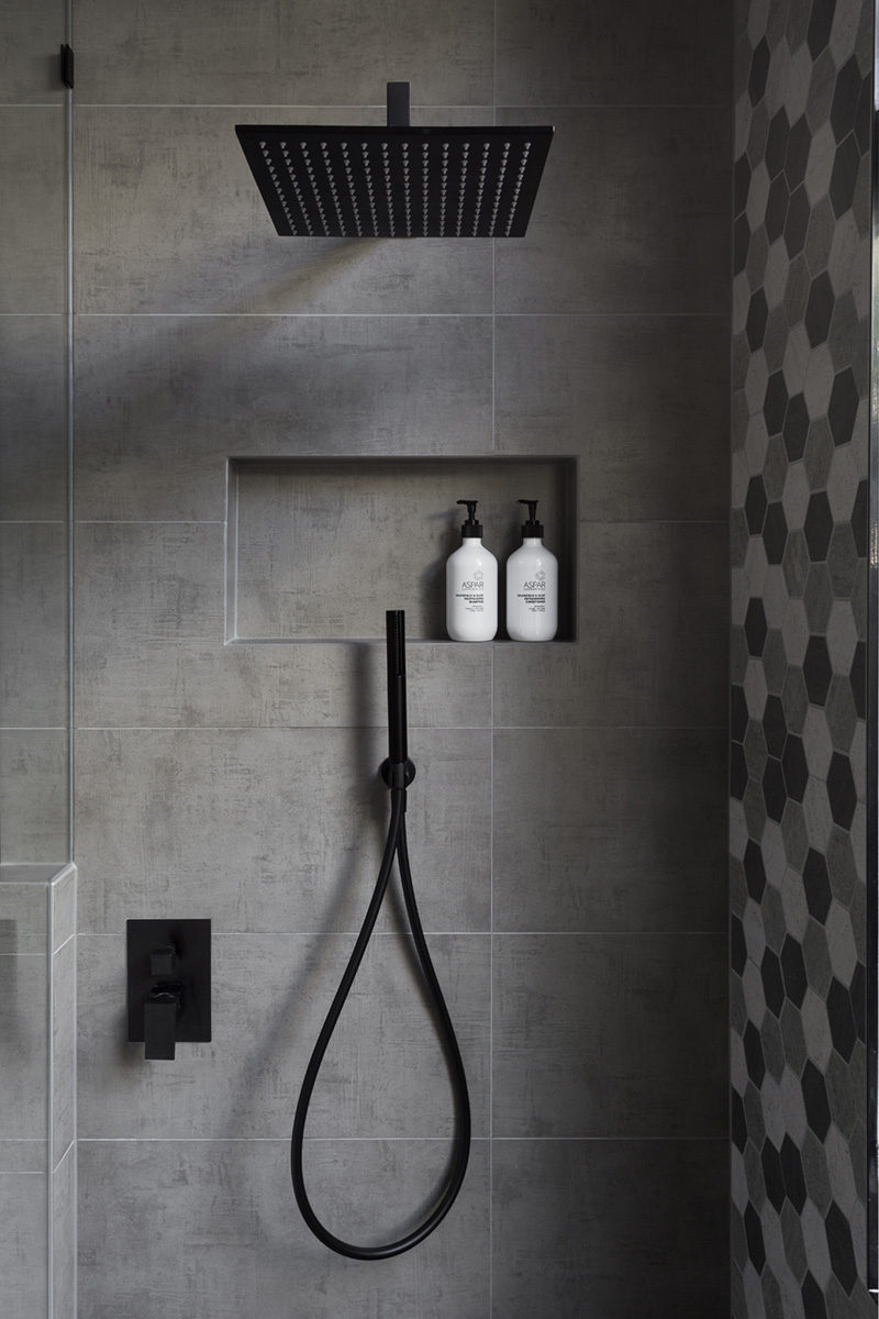 В этой современной ванной комнате есть душ с дождевой насадкой матового черного цвета и ручной душ, а также встроенная полка, выложенная плиткой.