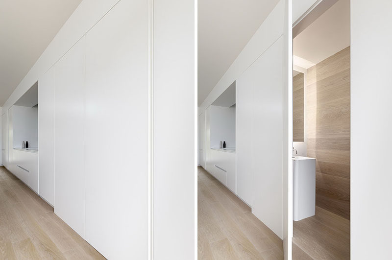 Обтекаемые минималистские белые кухонные Шкафы украшают стену в этом современном доме, за одной дверью спрятана дамская комната. #HiddenPowderRoom #KitchenDesign #WhiteCabinets 