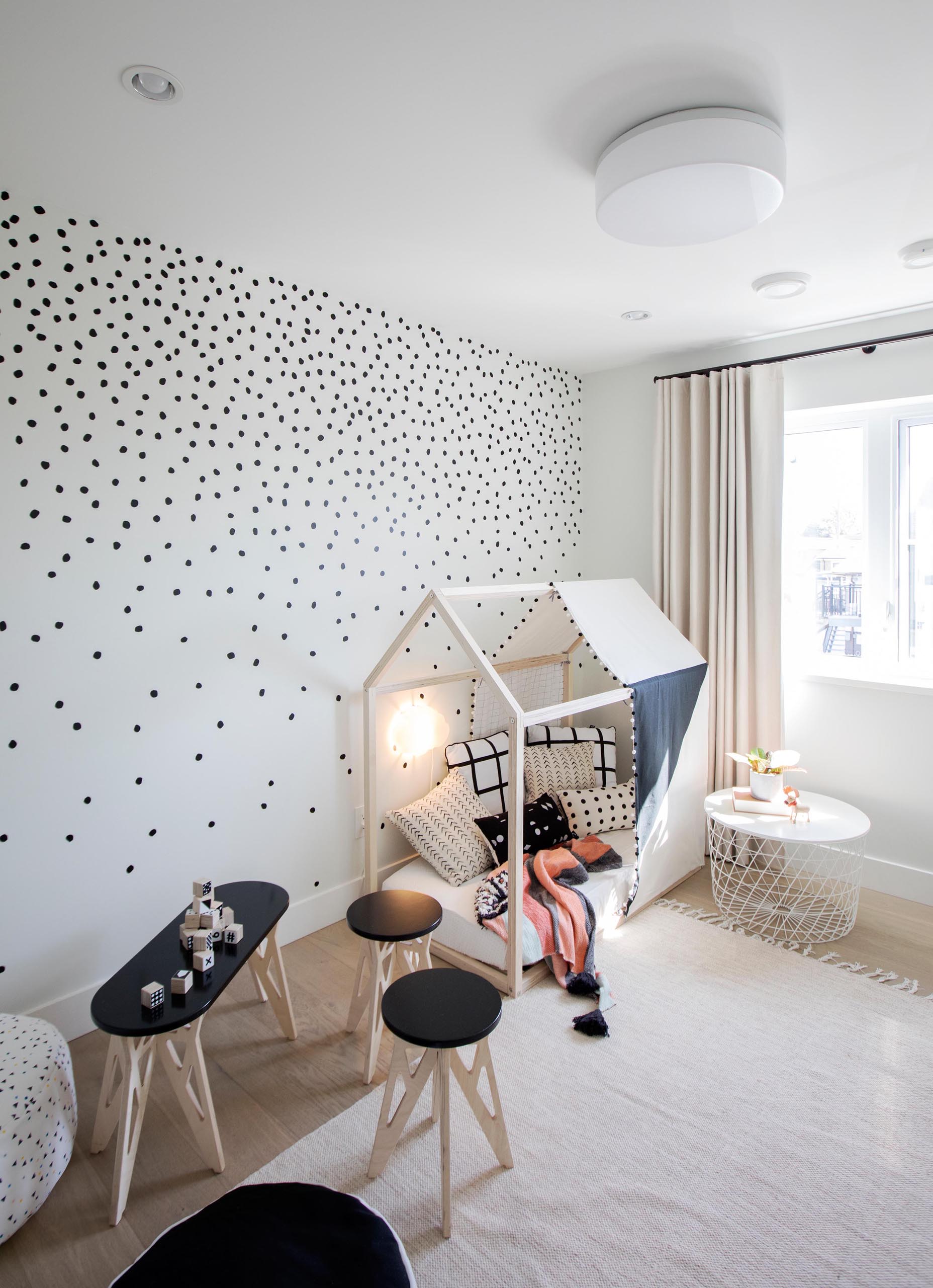Современная детская спальня имеет игривый вид, с узором в горошек на стенах, небольшой палаткой и детской мебелью со столом, стульями и пуфами.