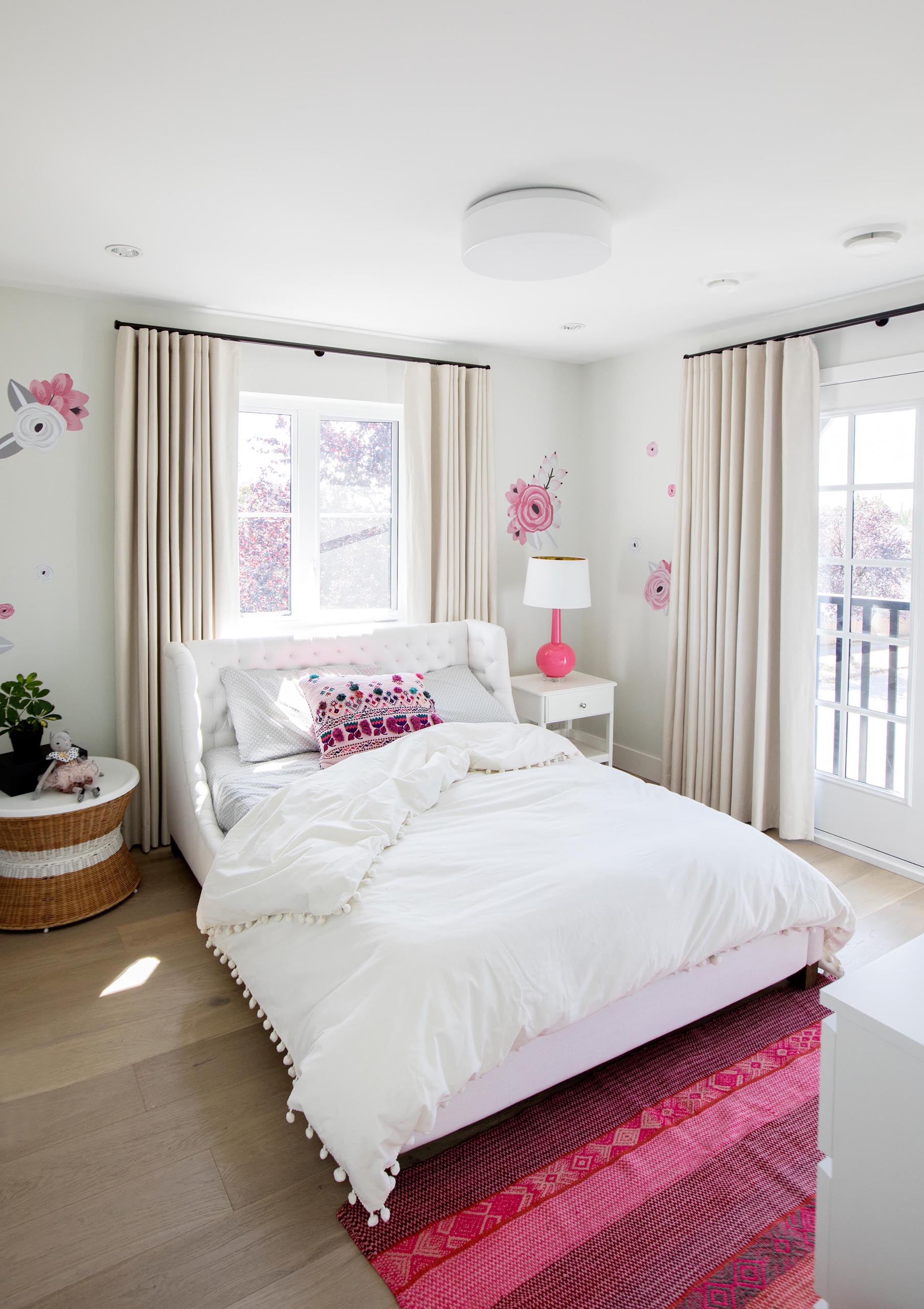 В этой спальне выбрана бело-розовая цветовая палитра. Цветочные акценты украшают стены, а в изголовье кровати расположен полосатый розовый коврик,