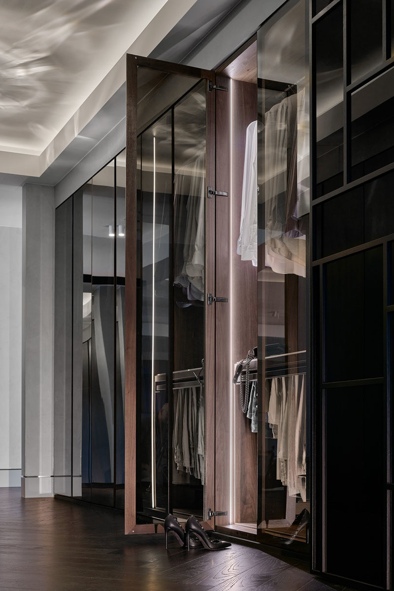 Гардеробная - Эта современная и большая гардеробная с люстрой и зеркальными шкафами создает роскошное пространство. Двери шкафа открываются, открывая вешалки и места для хранения вещей, подсвеченные скрытой подсветкой. #ModernCloset #WalkThroughCloset #ClosetDesign