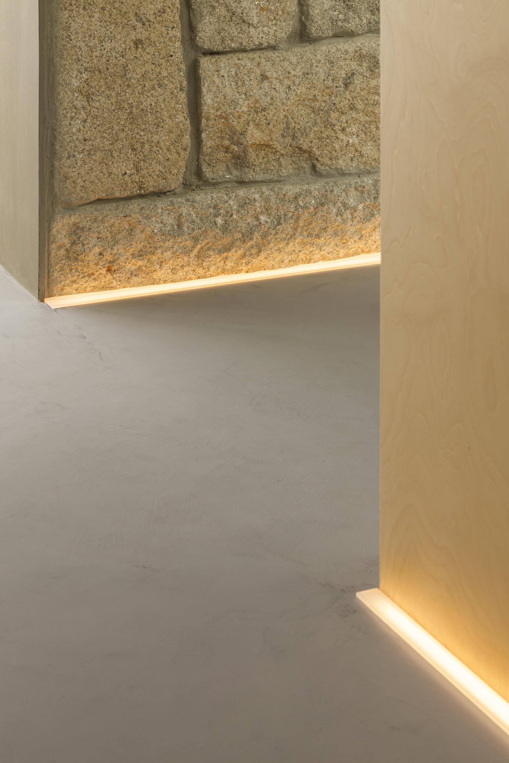 Коридор с каменными и деревянными стенами освещен светодиодной подсветкой на полу.