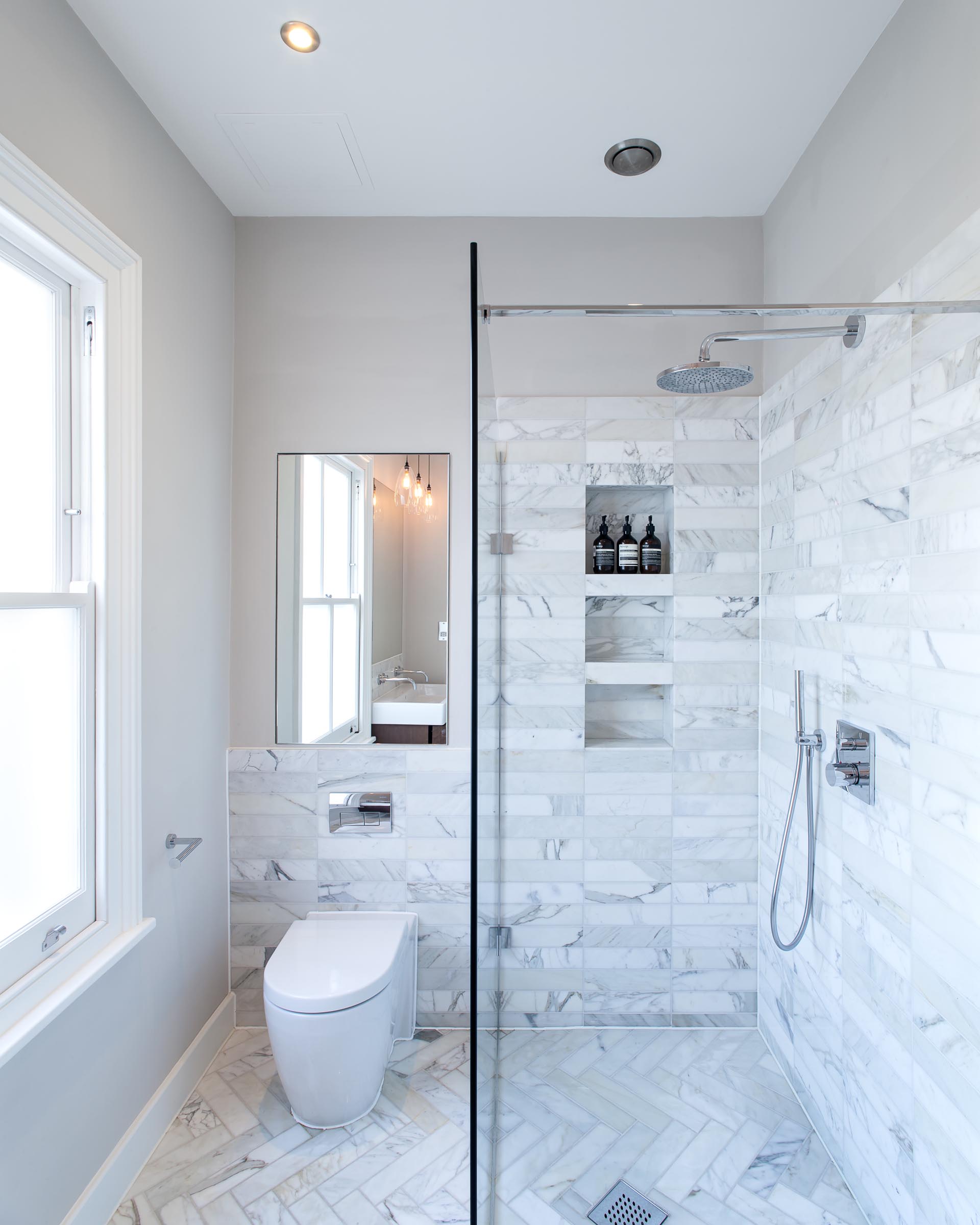 В этой современной ванной комнате пол и стены отделаны серой каменной плиткой, а в душе есть три встроенных душевых ниши.