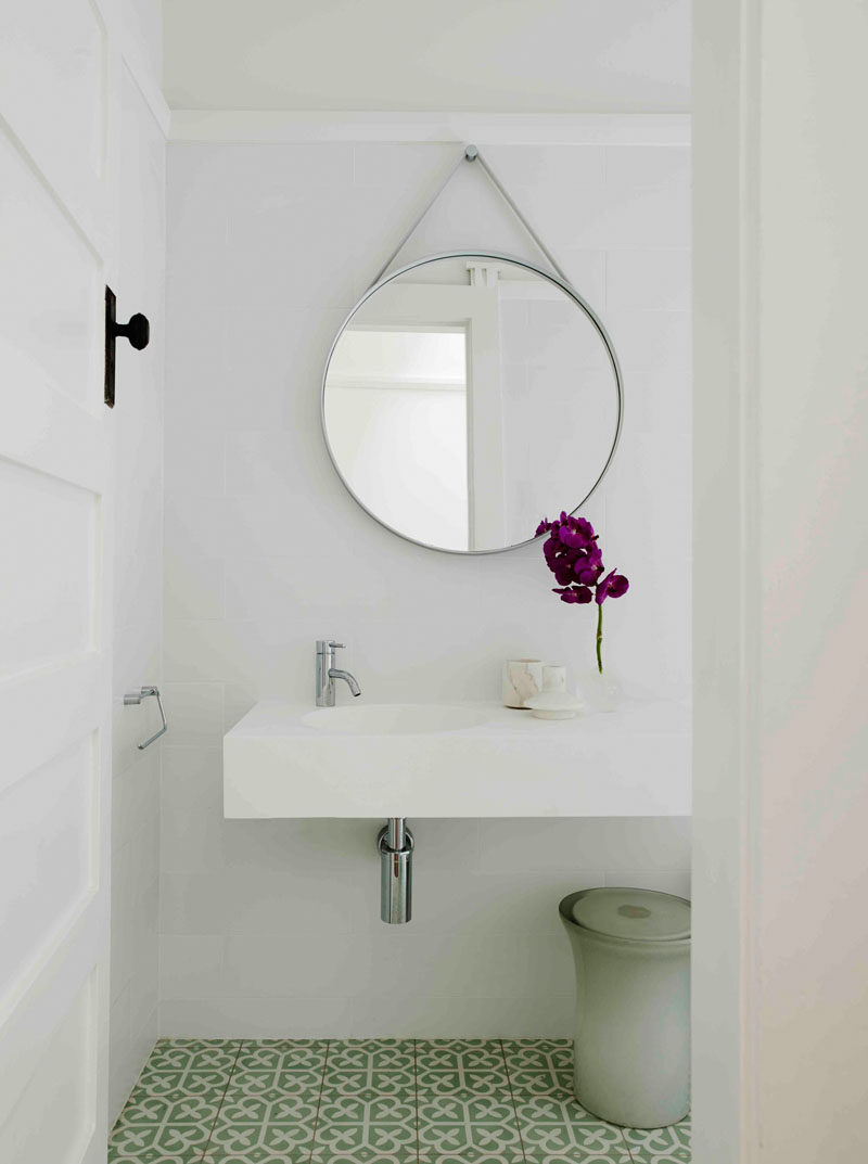 В этой современной ванной комнате есть круглое зеркало, висящее над минималистичным белым туалетным столиком, а узорная зелено-белая плитка покрывает пол, чтобы добавить немного цвета в пространство