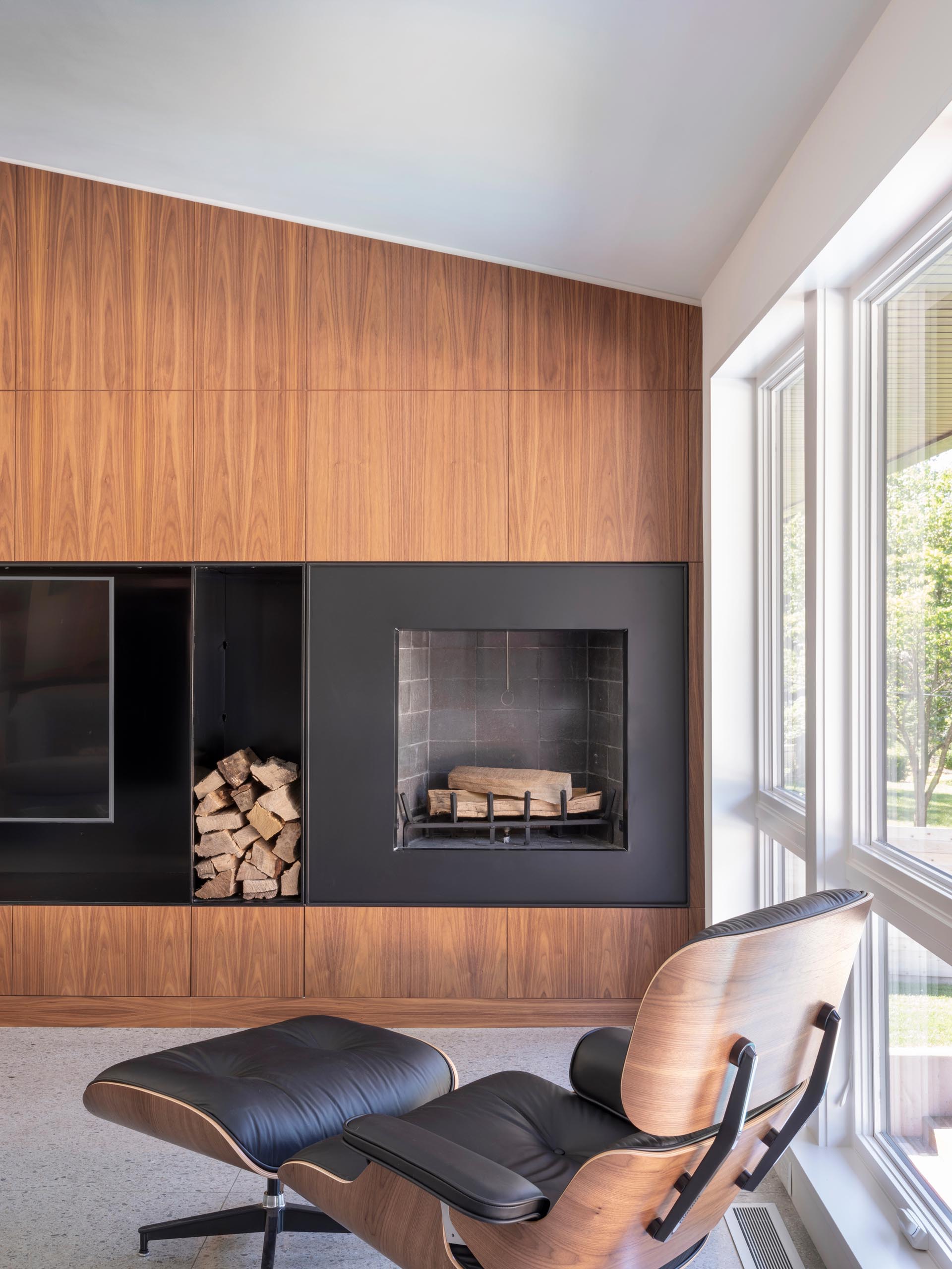 Современная гостиная с деревянной акцентной стеной, разделенной черной сталью, в которой есть телевизор и камин.