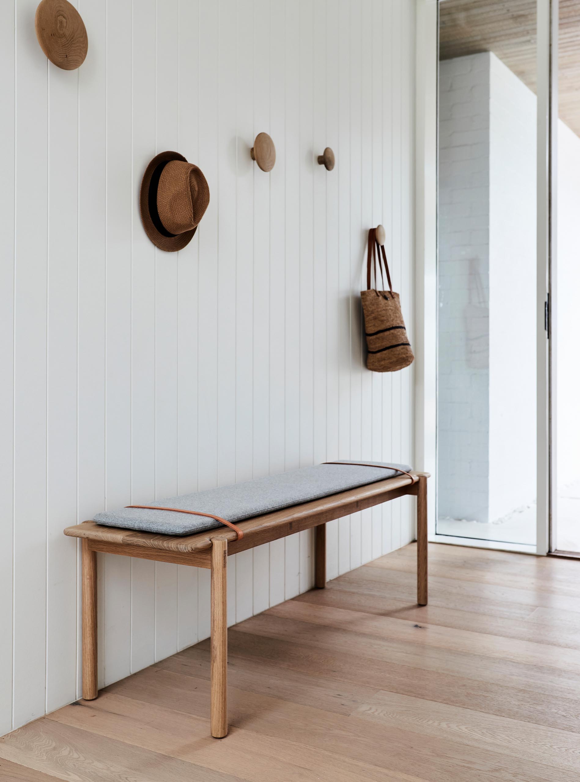 У этой современной прихожей белая стена, дубовый пол, простая скамья и круглые деревянные крючки на стенах.