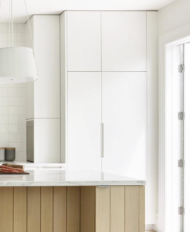 На этой современной кухне минималистичные белые шкафы перемещаются от пола до потолка, а небольшой гараж для бытовой техники спрятан в одной из боковых панелей. #WhiteCabinets #ModernKitchen #KitchenDesign #ApplianceGarage