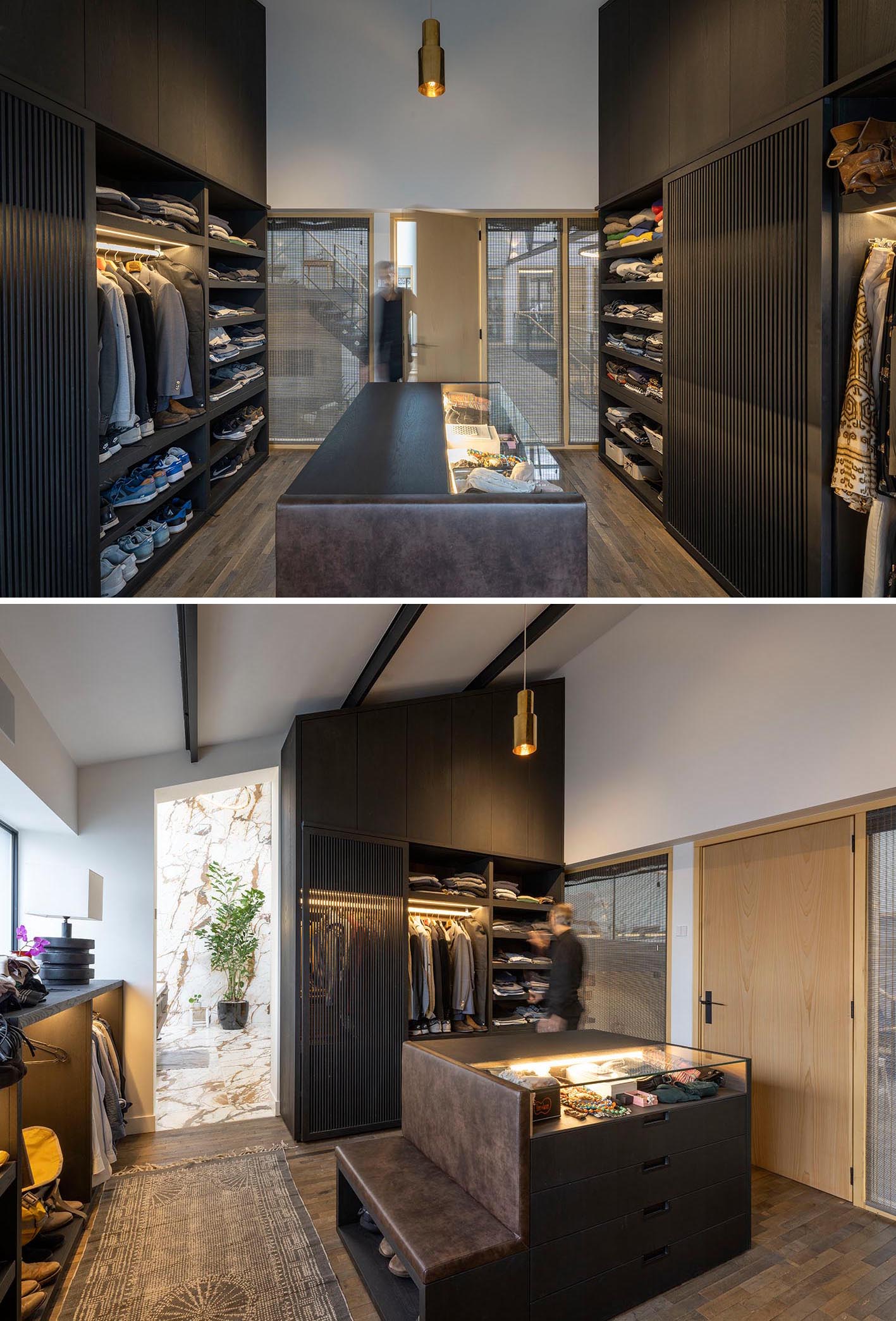 Современная гардеробная с черными шкафчиками, центральным островком аксессуаров и множеством открытых стеллажей.