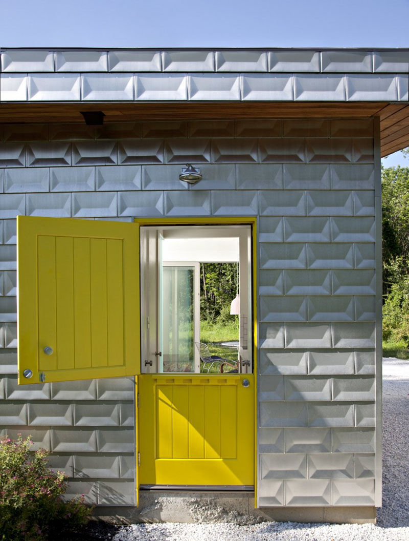 Желтая входная дверь в загородном стиле, которую можно открыть двумя способами, отражает цвет кирпичного матового алюминиевого фасада этого современного дома.