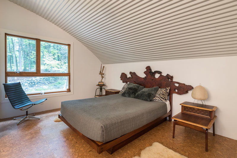 В этой современной спальне есть окно с видом на верхушки деревьев. и изогнутый потолок из-за формы хижины, в которой он находится. # Спальня 