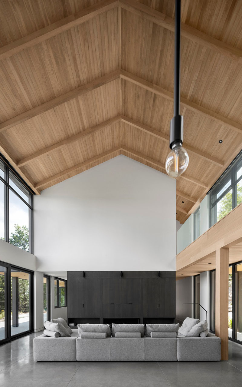 Современные идеи сарая - внутри этого современного сарая остроконечная крыша подчеркнута деревянным потолком, который привлекает взгляд вверх. В гостиной ряд шкафов включает телевизор и камин. #ModernBarnhouse # GabledRoof #ModernArchitecture #WoodCeiling