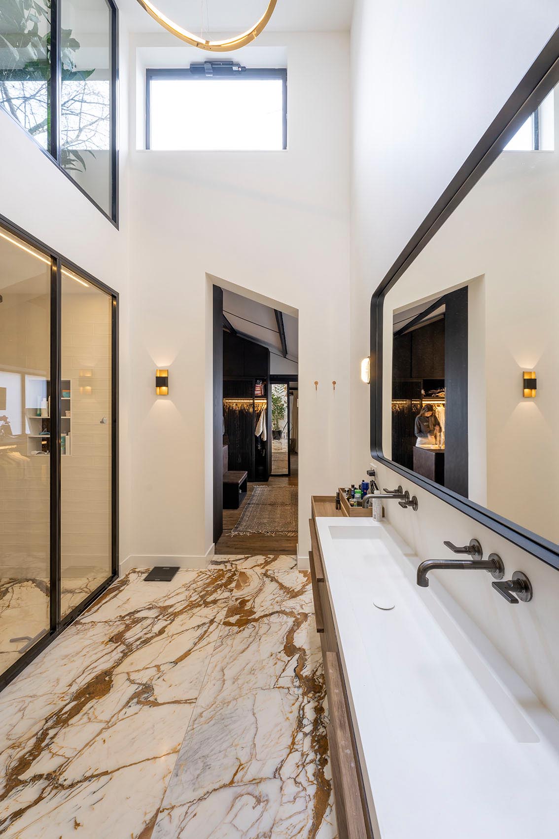 Современная ванная комната со стеклянной душевой кабиной и длинным тонким туалетным столиком с раковиной.
