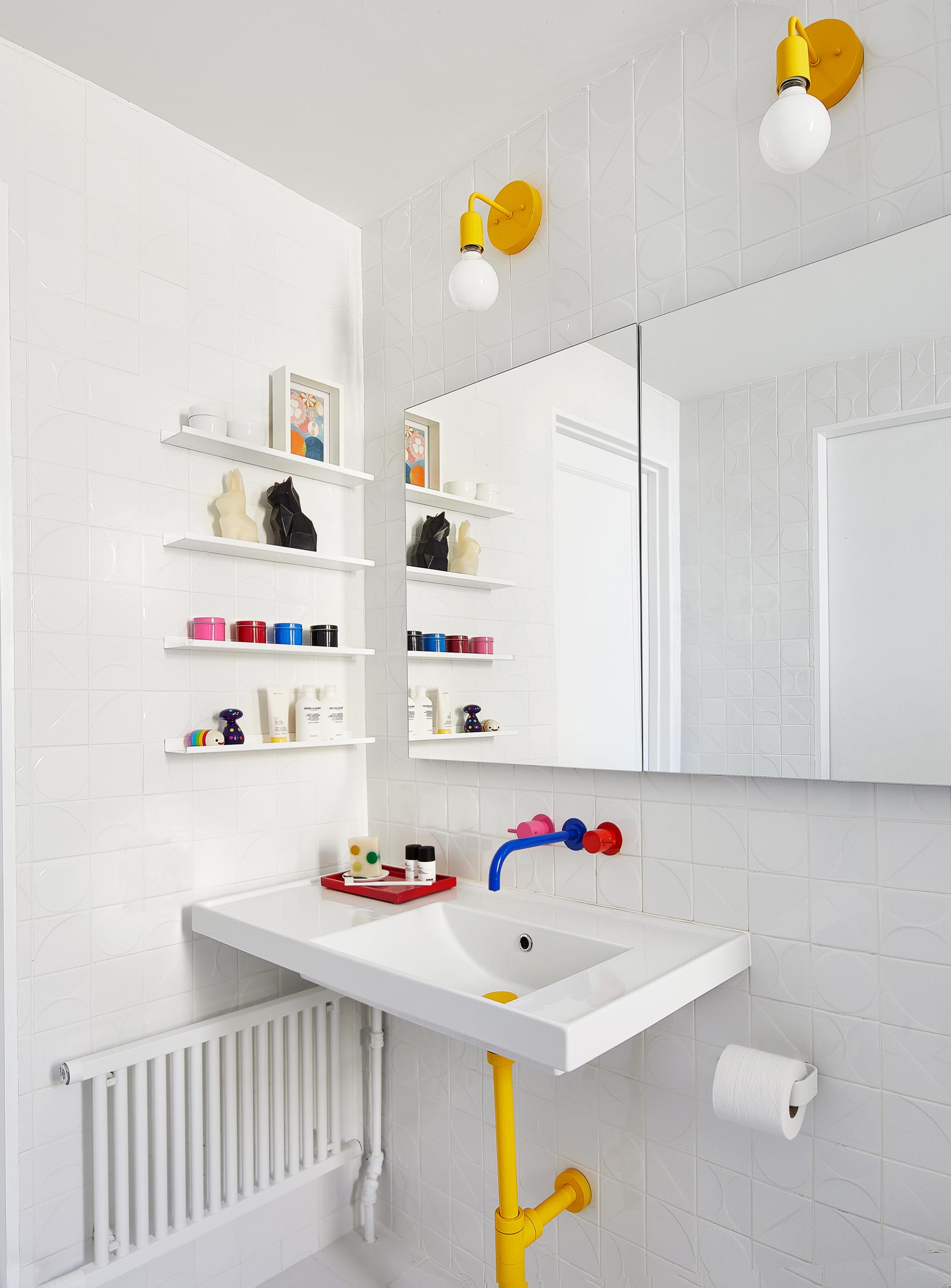 В этой детской ванной комнате смешанная ярко-розовая, желтая и синяя сантехника от VOLA сочетается с объемной настенной плиткой от Kho Liang и желтыми осветительными приборами от Barn Lighting.