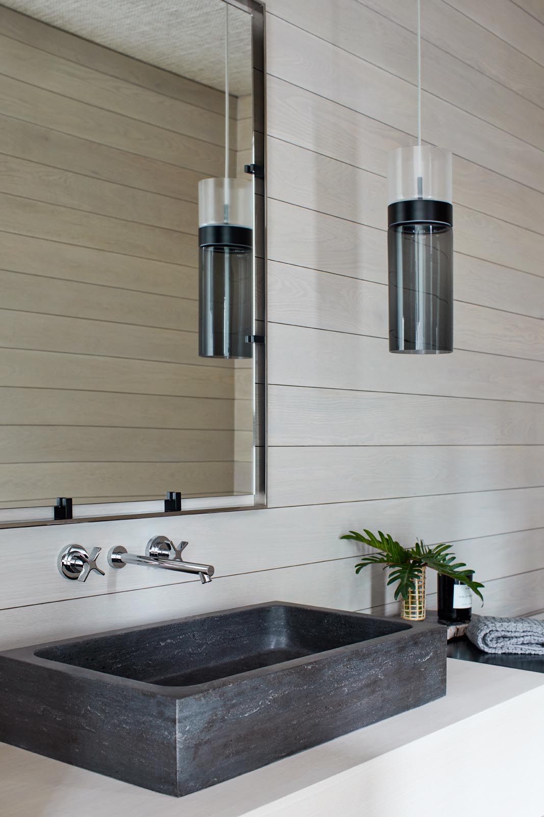 Современная ванная комната со стенами из светлого дерева, контрастирующими с черным подвесным светильником и раковиной.
