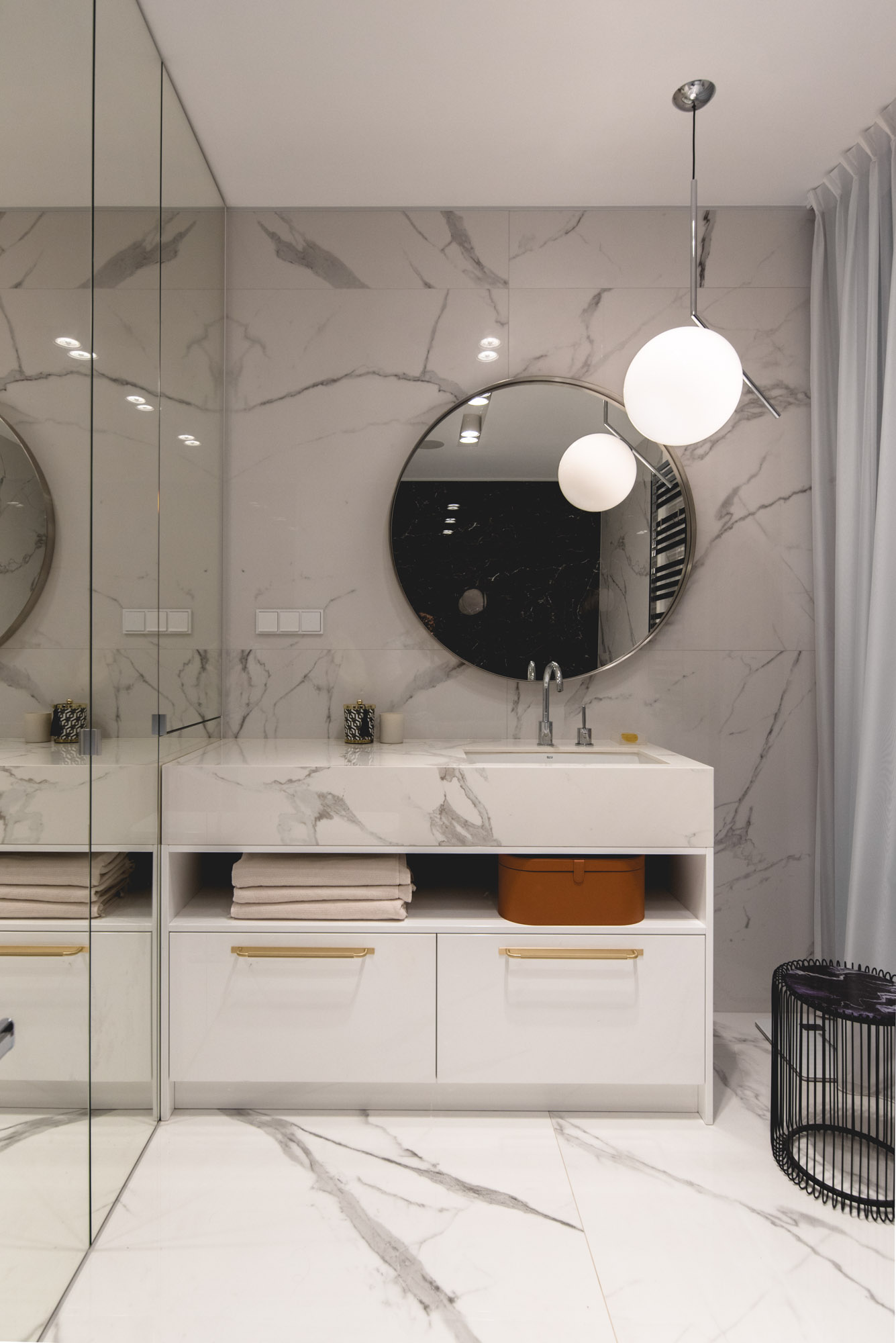 В этой современной ванной комнате камень покрывает стены и туалетный столик, а круглое зеркало и подвесной светильник добавляют изогнутый элемент.