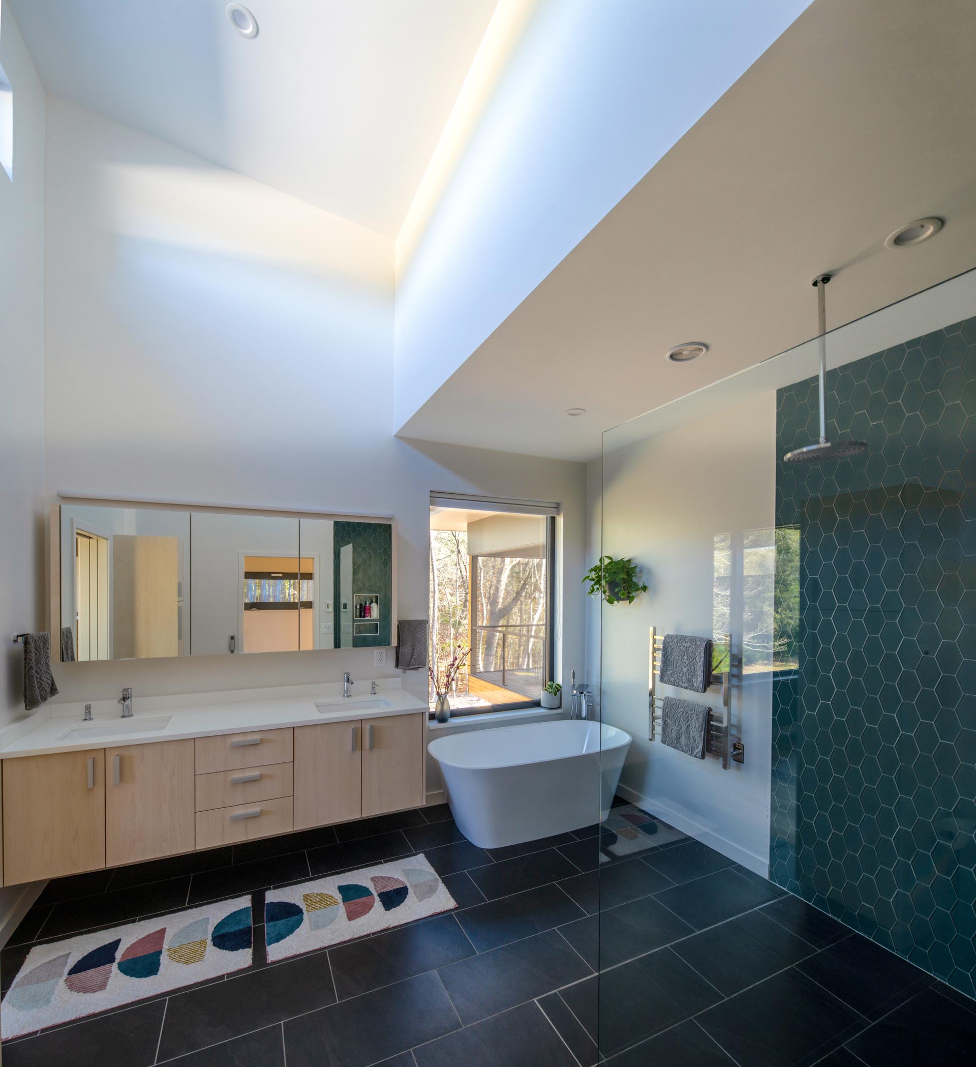 Эта главная ванная комната, похожая на спа, имеет высокий потолок, черную плитку на полу, двойную раковину, глубокую ванну и душ с акцентом на стене из шестиугольной плитки.