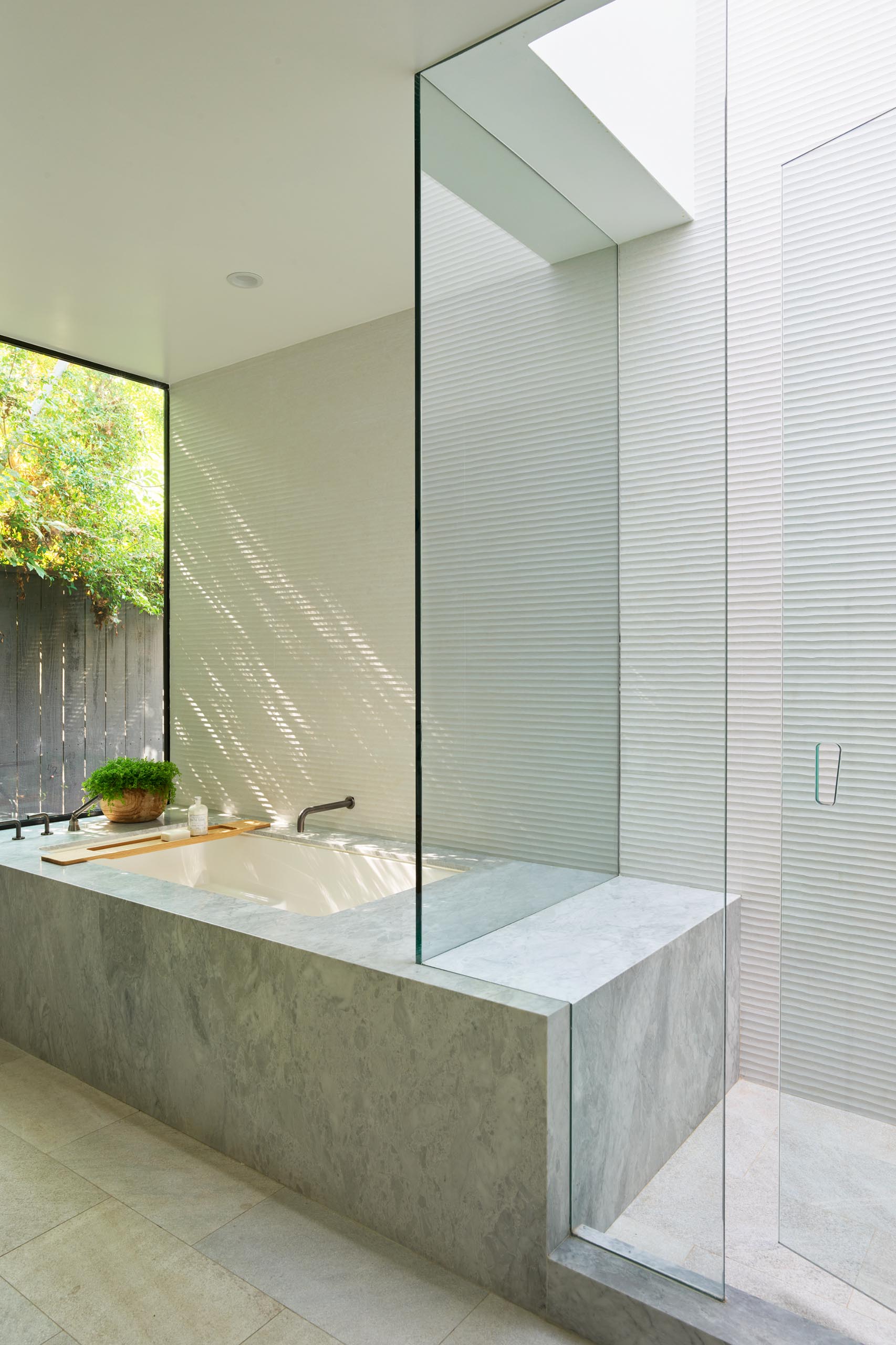 Современная ванная комната с душем и встроенной ванной с видом на растения на улице.