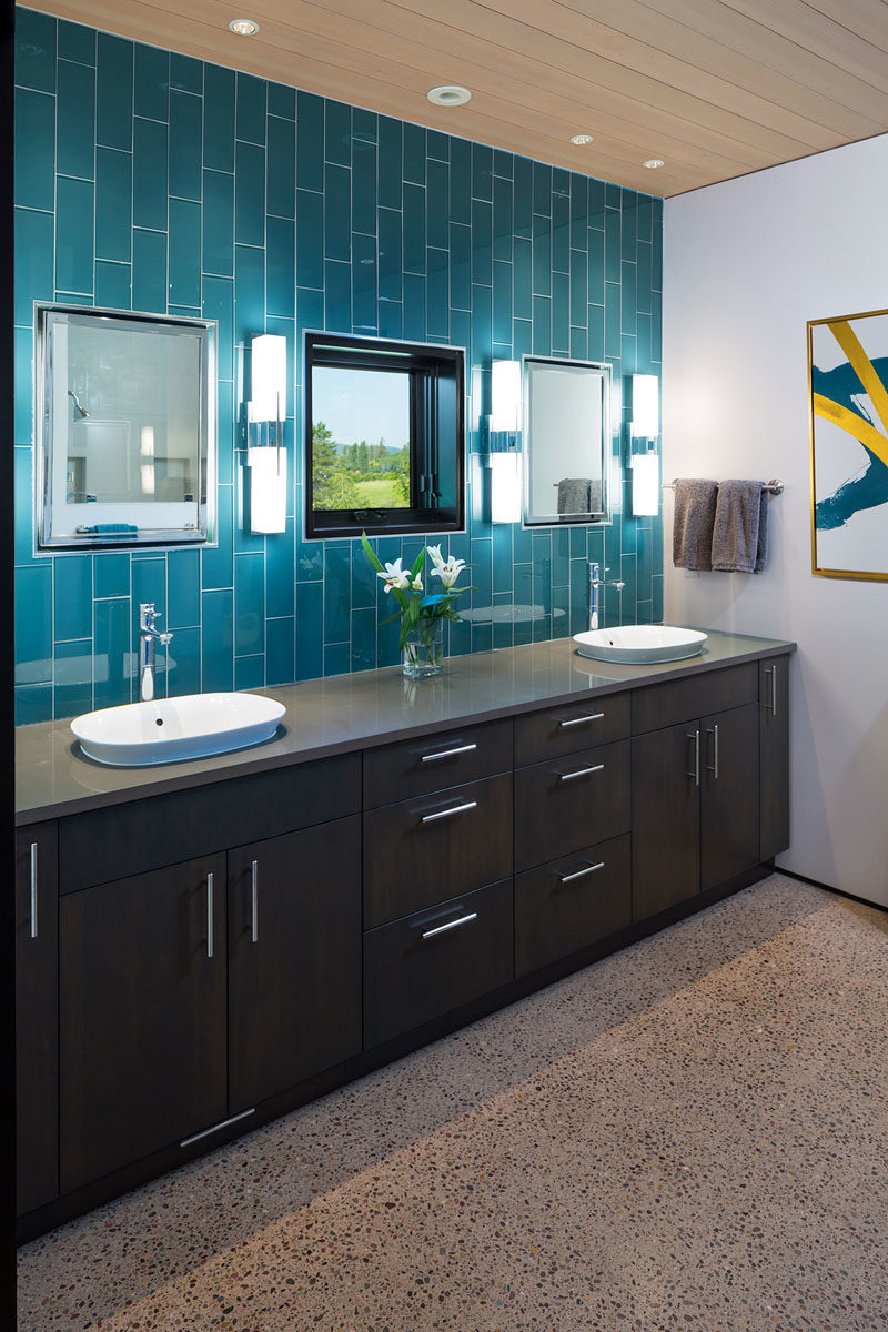 Идеи для ванных комнат - в этой современной ванной голубая плитка, уложенная вертикально, привлекает внимание к высоте комнаты. На туалетном столике из темного дерева от стены до стены достаточно места для двоих, а зеркала расположены по обе стороны от зеркала. # ВанныеИдеи # СовременныеВанные # Голубая плитка # ДеревянныйПотолок