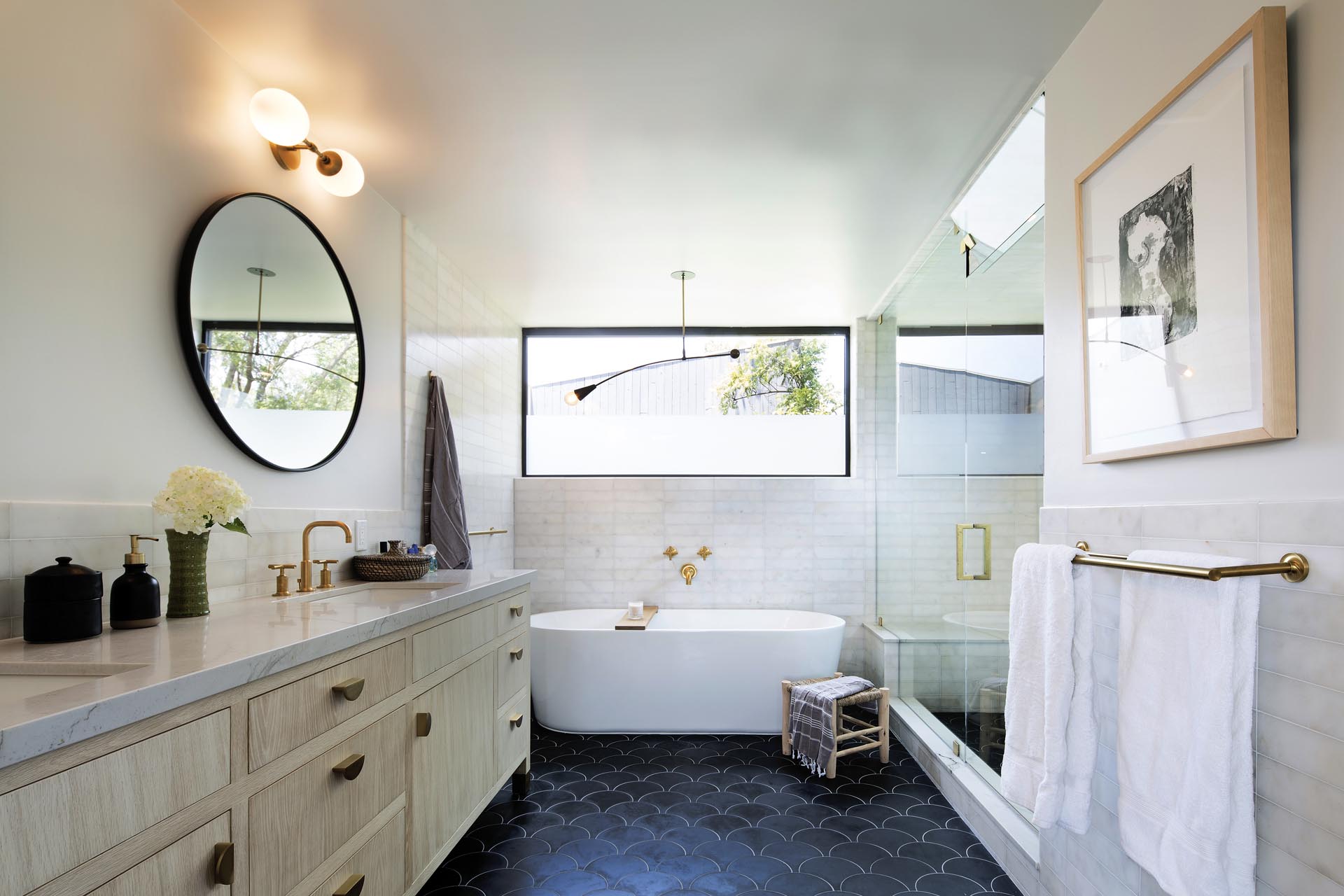 В этой современной ванной комнате есть двойная раковина с круглыми зеркалами, отдельно стоящая ванна и застекленная душевая кабина.