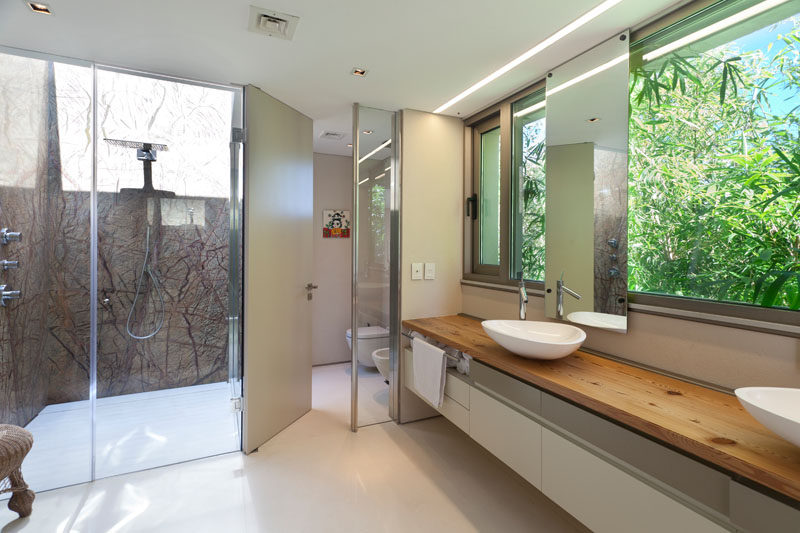  В этой современной главной ванной комнате большой деревянный туалетный столик выходит в сад, застекленная душевая кабина имеет потолочное окно. #MasterBathroom #DoubleVanity #GlassEnclosedShower #InteriorDesign 
