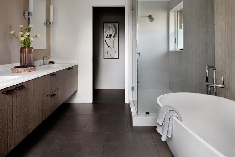 В этой современной главной ванной комнате темная плитка контрастирует со светлыми стенами, отдельно стоящей ванной и белыми столешницами парящей деревянной раковины. # МодернМастерВанная # СовременнаяВанная # Дизайн ванной