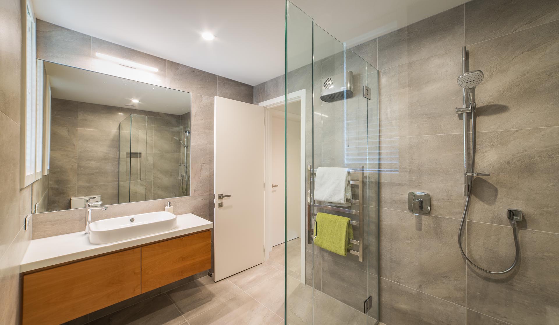 Современная ванная комната с плиткой большого формата, деревянной раковиной и белой столешницей с подходящей раковиной.