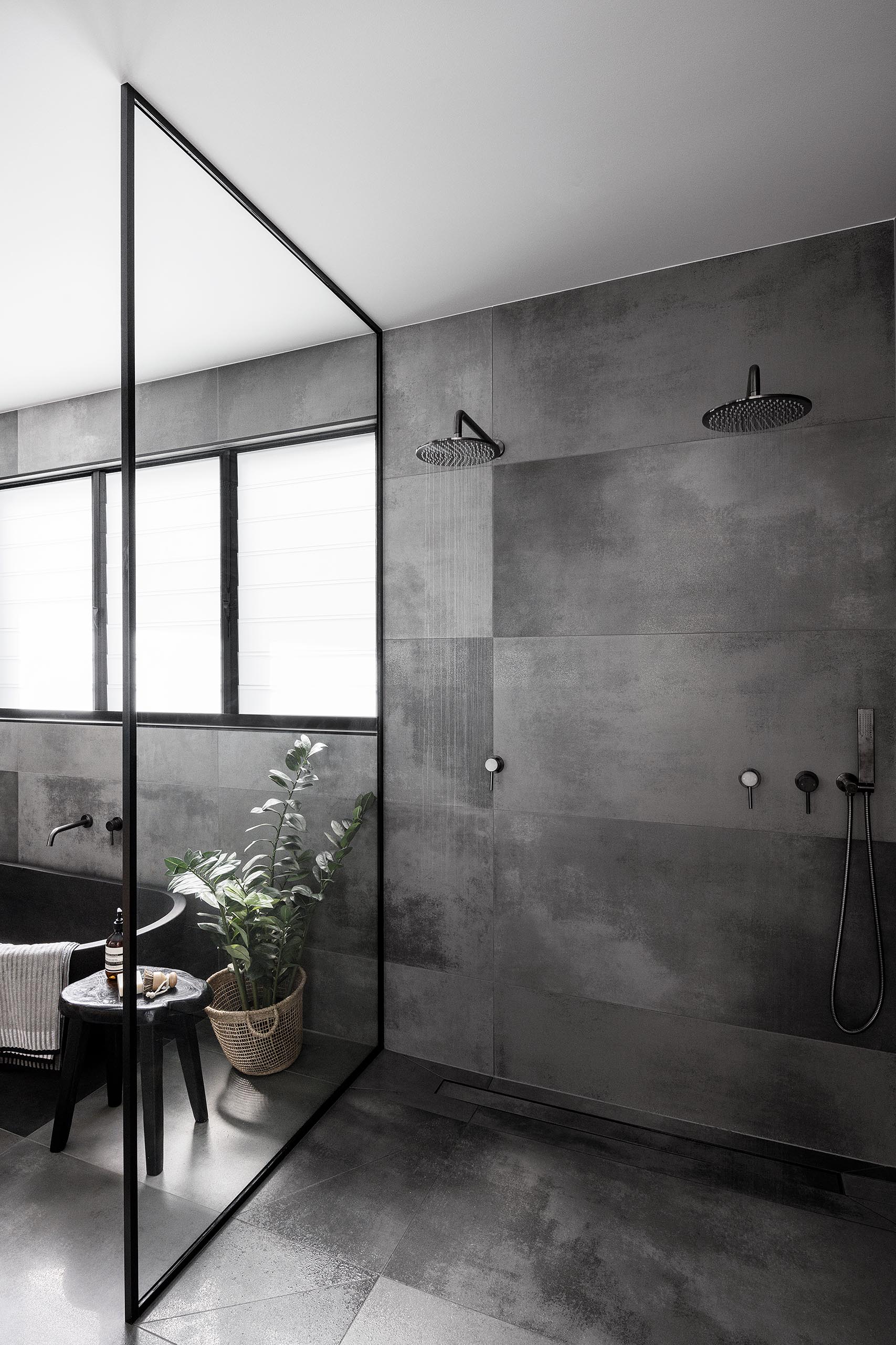 Современная ванная комната со стеклянной душевой перегородкой в ​​черной рамке, серой плиткой большого формата и двумя душевыми лейками.