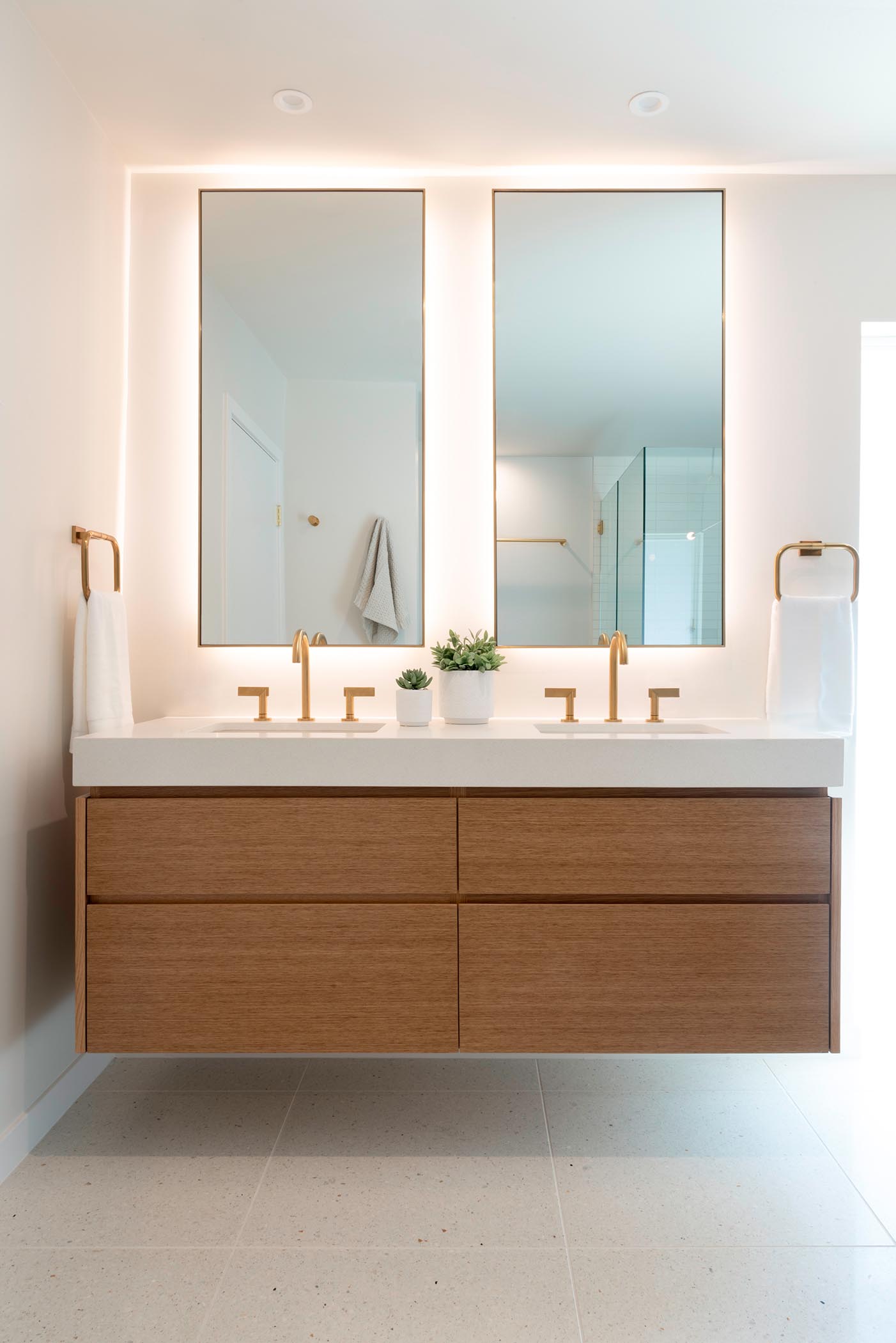 В этой современной ванной комнате есть настенный деревянный туалетный столик с индивидуальными зеркалами с подсветкой и латунные светильники.